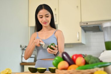 Evdeki mutfakta sağlıklı salata yaparken avokado kesen genç ve güzel bir kadın. Diyet ve sağlıklı yaşam tarzı kavramı.