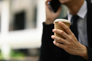 İş adamının elinde hazır kahve fincanı tutmasına ve dışarıda cep telefonuyla konuşmasına odaklanın.