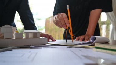 Mimarların, meslektaşlarıyla proje üzerinde çalışırken pusulayı kullanarak bir plan üzerinde ölçüm yaparken yakın plan çekimleri..