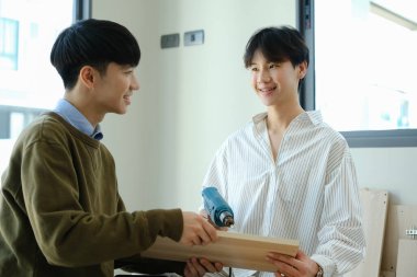 Neşeli eşcinsel çift yeni evlerinde tornavidayla mobilya monte ediyorlar..