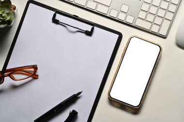 Beyaz ekranlı akıllı telefon, beyaz ofis masasında pano ve gözlük. Üst manzara, düz uzanma.