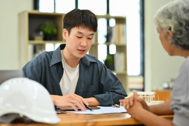 Gülümseyen erkek mimar ofiste orta yaşlı kadın ev sahibi yenileme planı gösteriyor..
