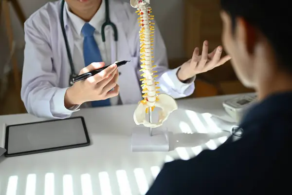 Experienced male orthopedist giving consultation about scoliosis or spinal problems during medical exam.