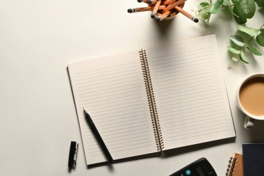 Beyaz ofis masasında kalem, kahve fincanı ve kalem tutacağı olan boş bir defter. Metin için boşluk olan üst görünüm.