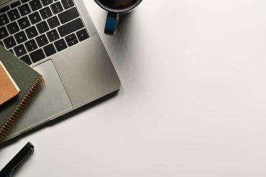 Laptop, not defteri ve beyaz ofis masasında bir fincan kahve. Düz konum, metin için kopyalama alanı olan üst görünüm.