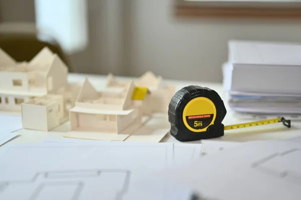 A measuring tape, architectural model and blueprints on desk. Building, construction and architect concept.