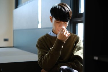 Üzgün, depresif, pencerenin kenarında oturan genç adam, işten dolayı stresli, endişeli, kalbi kırık. Akıl sağlığı kavramı.