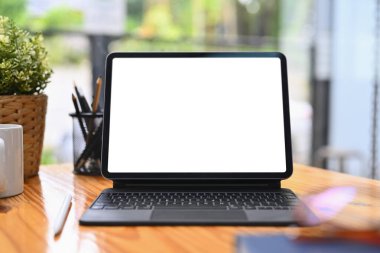 Boş ekranlı dijital tabletin ön görüntüsü, ahşap ofis masasında kahve fincanı ve kalem tutacağı..
