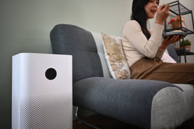 Oturma odasında filtre ve temizlik için hava temizleyicisi var. Arka planda kadın koltukta dinlenirken PM2.5 tozu kaldırılıyor..