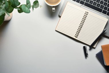 Üst görünüm boş not defteri, dizüstü bilgisayar, kahve fincanı ve beyaz ofis masasında saksı bitkisi. Metnin için boşluk kopyala.
