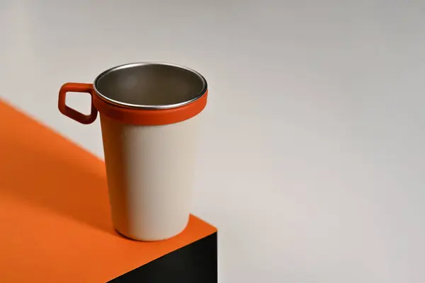 White ceramic travel cup with silicone holder on orange table. Tumbler beverage container and Eco friendly concept.