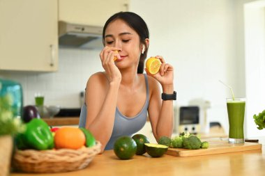 Güzel genç bir kadın taze limon koklarken kapalı gözlerle mutfakta sağlıklı yemek yapmak için gerekli malzemeleri hazırlıyor..