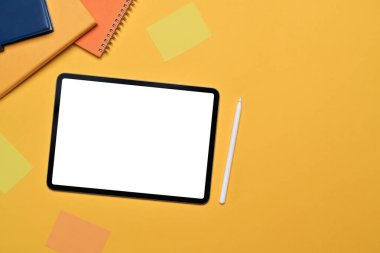 Dijital tablet, stil kalemi, defter ve sarı arkaplanda yapışkan notlar. Üst manzara, düz uzanma.