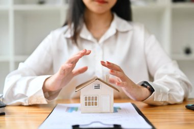 Genç kadın elleri küçük ev modelini koruyor. Emlak sigortası ve güvenlik kavramı.