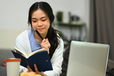 Güzel genç Asyalı kadın dizüstü bilgisayar kullanıyor ve programı veya el yazısını kontrol ediyor. Önemli bilgiler..