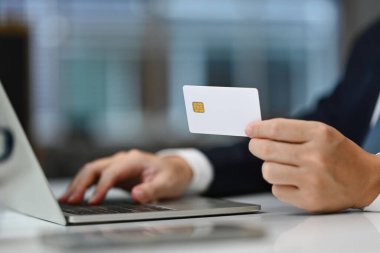 Kredi kartı tutan ve dizüstü bilgisayar kullanan, alışveriş yapan, web mağazalarının ödemelerini yapan, faturaları ödeyen bir adam..