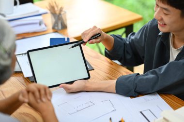 Gülümseyen mimar dijital tablet ekranı işaret ederek ev yenileme planını müşteriye açıklıyor.