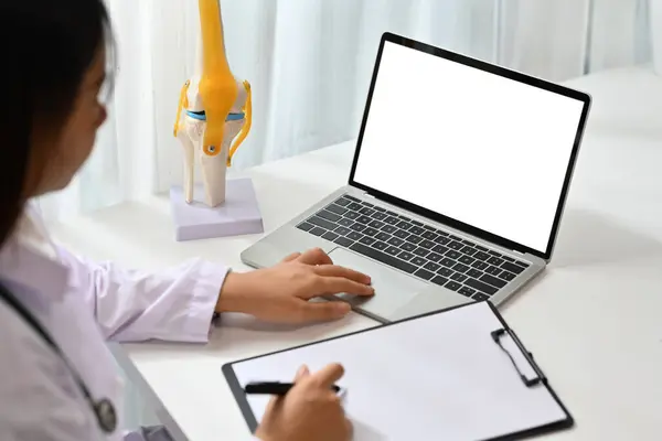 Side view of female doctor in white coat watching online medical webinar seminar training on laptop computer.