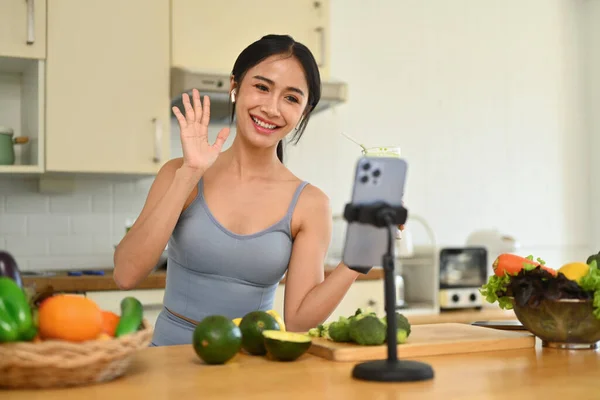 Fit young asian girl drinking green smoothie and recording her blog about healthy food on smartphone at the kitchen.