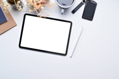 Beyaz ofis masasında dijital tablet, stilus kalem, defter ve kahve fincanının üst görünümü.