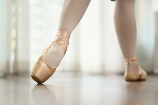Ballerina feet in pink pointe shoes dancing on wooden floor. People, dance art, education and flexibility concept.