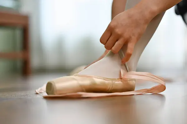 Closeup ballerina tying pointe shoes in dance studio. Art, dance, people and inspiration concept.