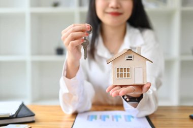 Evin modelini ve anahtarlarını tutan gülümseyen kadın. Emlak, kredi, ipotek ve sigorta kavramı.