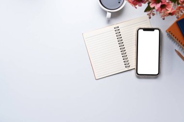 Boş ekranlı akıllı telefon, boş not defteri ve beyaz masada bir fincan kahve. Üst manzara, düz uzanma.
