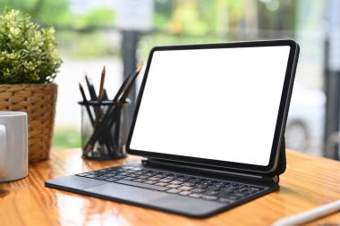 Boş ekranlı dijital tablet, kalem tutacağı, kahve fincanı ve ahşap masadaki saksı..