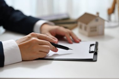 Emlakçı elinde kalemle kontrat belgelerine bakıyor. Gayrimenkul, mortgage, kredi ve sigorta.