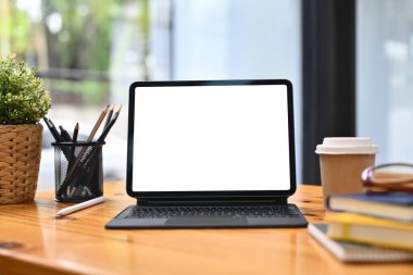 Dijital tablet, kalem tutacağı, kahve fincanı ve kitap ahşap masada. Reklam için beyaz ekran.