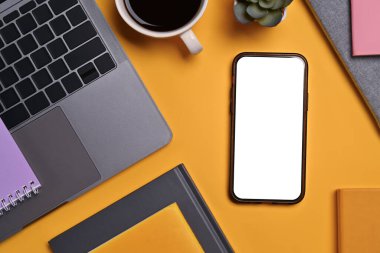Düz konum, üst görünüm akıllı telefon boş ekran, dizüstü bilgisayar, bir fincan kahve ve sarı arkaplan üzerine kitap.