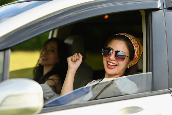 Cheerful female friends singing and dancing in car on road trip, enjoy holidays together.