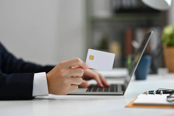 Side view of businessman holding credit card and using laptop, making online payment purchase or transferring money in website.