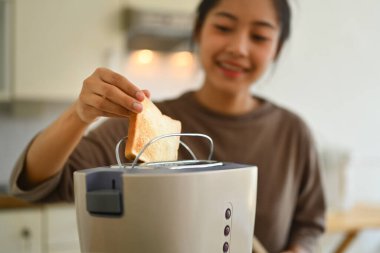 Sabah kahvaltıda ekmek kızartma makinesiyle ekmek kızartan genç bir kadın..