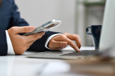 Akıllı telefon tutan ve dizüstü bilgisayarda yazan işadamlarının yakın plan çekimleri.