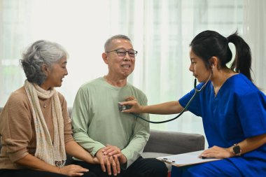 Steteskop kullanan kadın doktor ev ziyareti sırasında yaşlı hastaların kalp atışlarını dinliyor..