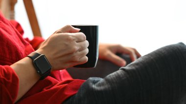 Genç adam sıcak kahve içiyor dinleniyor ve boş vakitlerini oturma odasında geçiriyor..