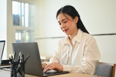 Çekici Asyalı kadın çevrimiçi pazarlamada çalışıyor, iş yerinde dizüstü bilgisayar kullanıyor..