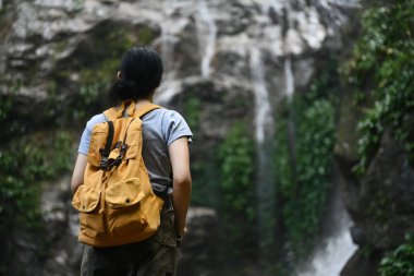 Sırt çantalı bir kadının inanılmaz tropikal şelalenin tadını çıkarışını izliyoruz. Seyahat, macera ve aktif yaşam konsepti.