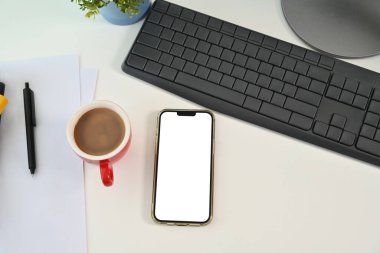 Beyaz ekranlı üst görünüm akıllı telefon, beyaz ofis masasında kahve fincanı ve klavye..