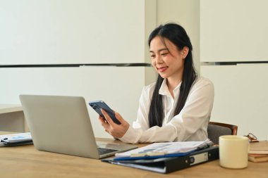 Güzel iş kadını işe ara veriyor ve ofis masasında cep telefonu kullanıyor..