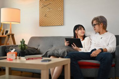 Birlikte oturma odasında dinlenirken dijital tablet kullanan mutlu genç çift..