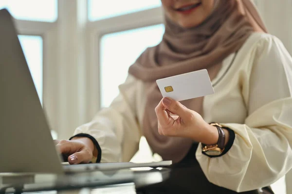 Happy muslim woman holding credit card using laptop doing online banking transaction or shopping in online store.
