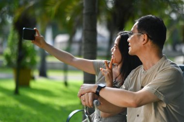 Yetişkin kız ve babanın parkta akıllı telefondan selfie çektiği güzel bir an..