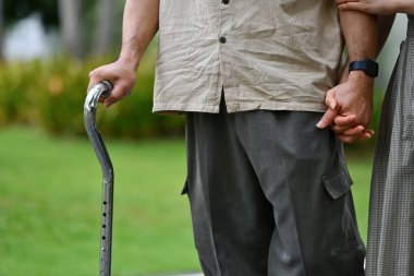 Genç yetişkin bir kızla parkta bastonla yürüyen yaşlı bir adamın kırpılmış görüntüsü..