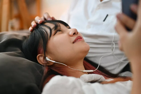 Pleasant young woman using mobile phone and listening music new playlist on couch with her boyfriend.