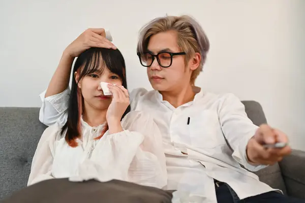 Young couple watching drama series on television in living room while spend weekend together at home.