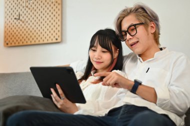 Rahat genç çift evdeki kanepede otururken dijital tablette internette geziniyor..