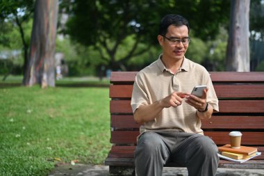 Tasasız orta yaşlı bir adamın halka açık bir parkta cep telefonu kullanarak gözlük takması..